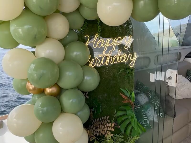 Decoração de aniversário na lancha com balões verdes e letreiro Happy Birthday neon