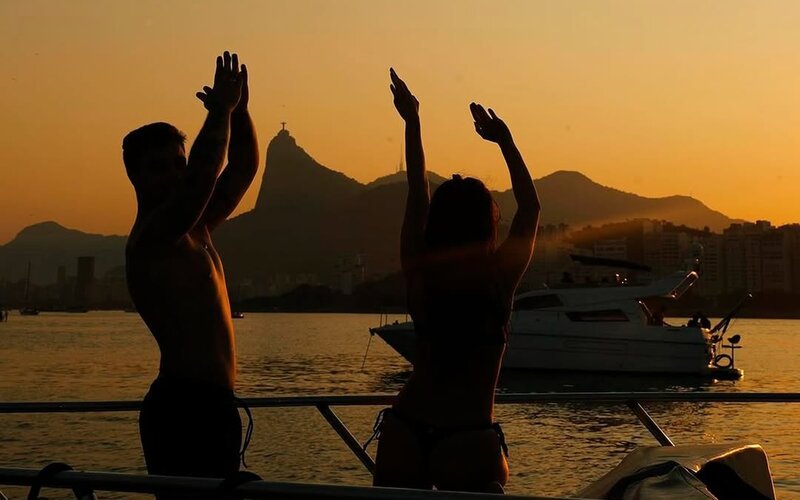 Casal em silhueta ao pôr do sol com Cristo Redentor ao fundo na lancha